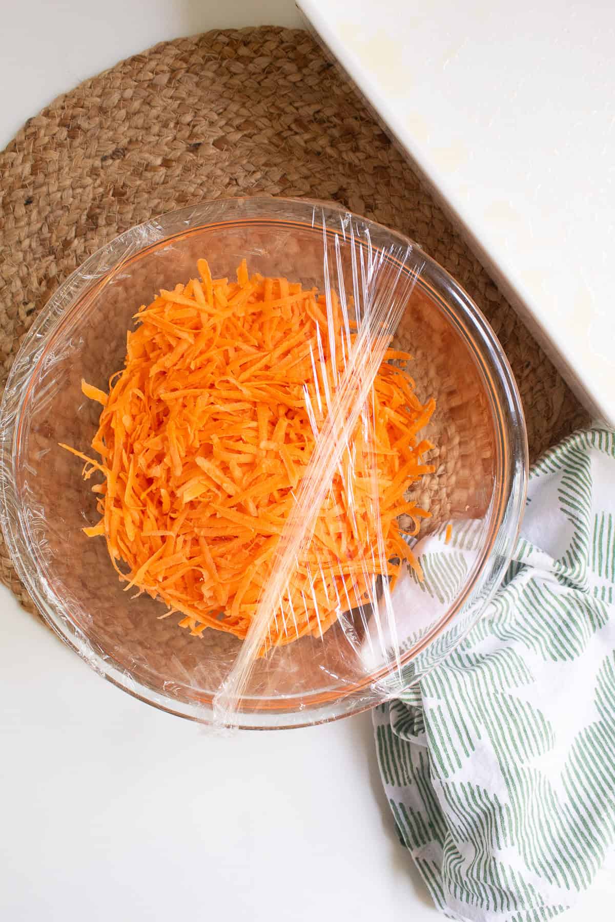 Shreds of sweet potato are covered with plastic wrap in a glass bowl.