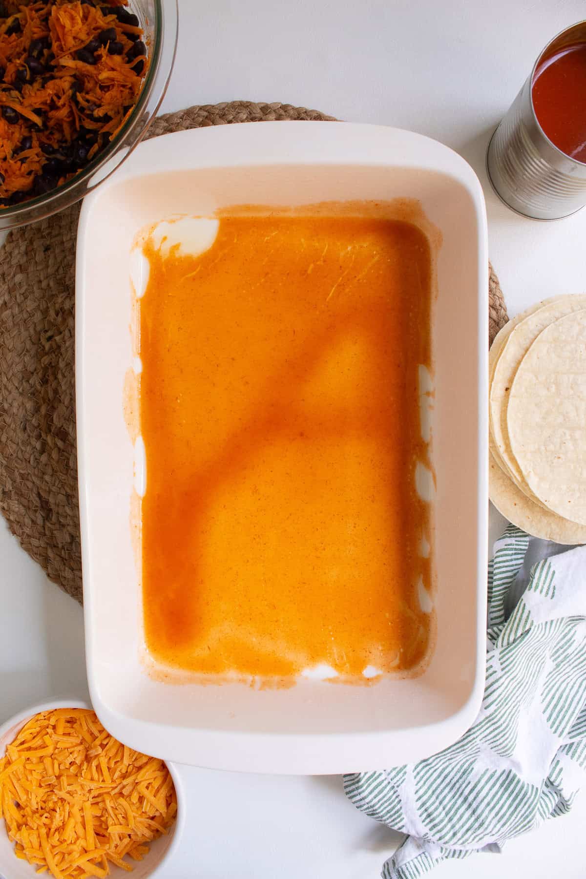 A thin layer of enchilada sauce coats the bottom of the casserole dish.