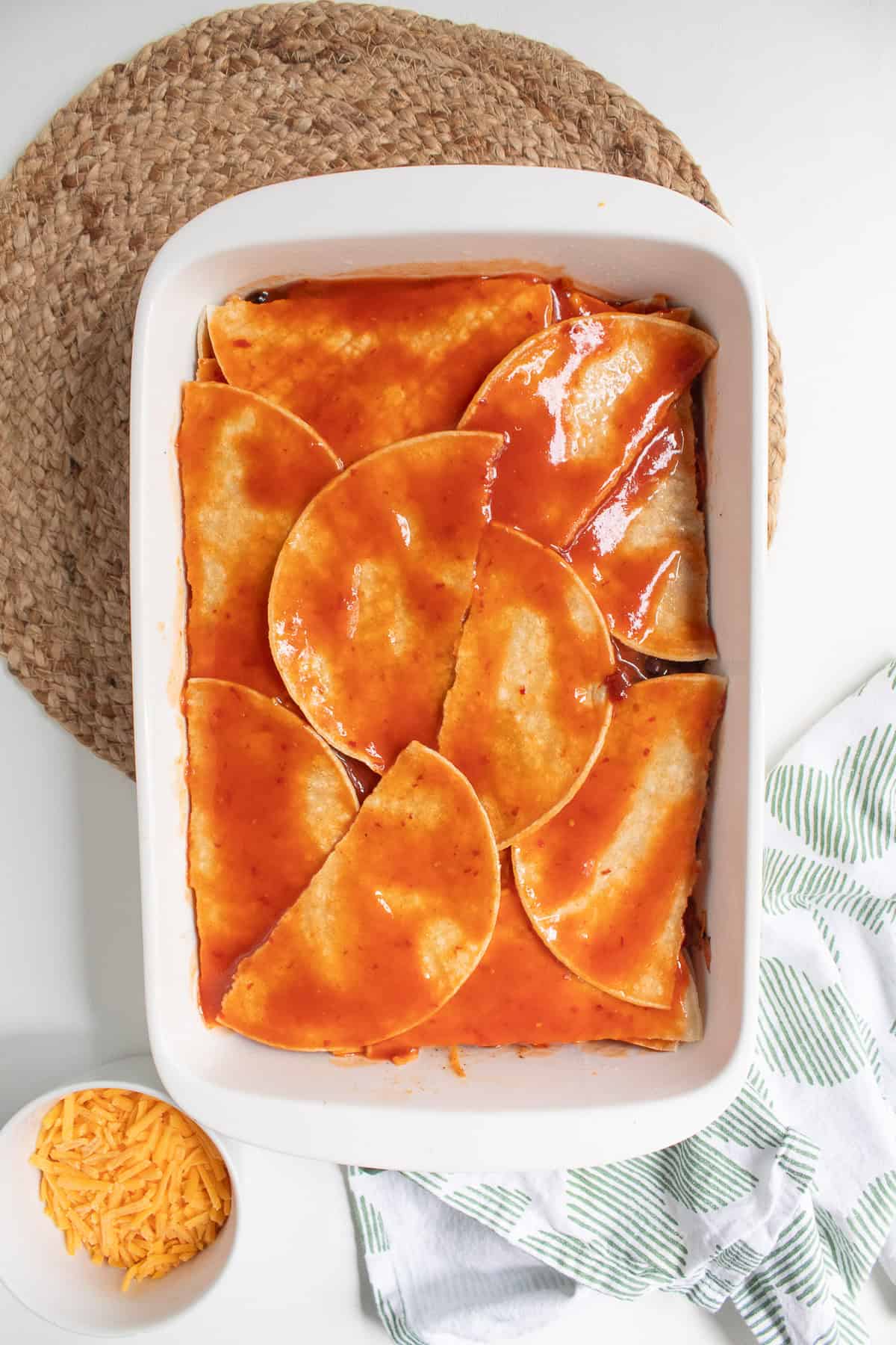 Enchilada sauce covers the top layer of tortillas.