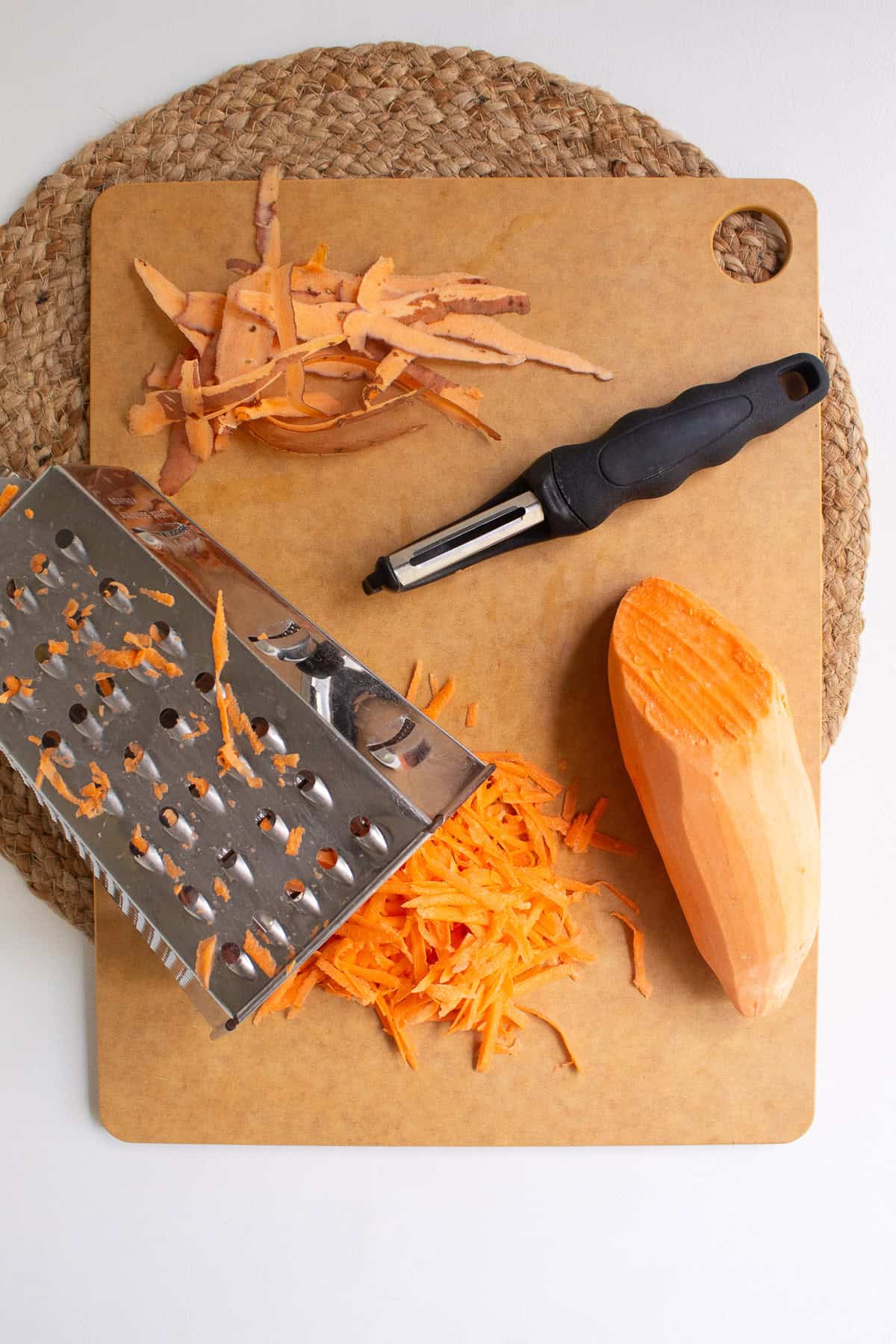 A sweet potato is peeled and shredded on the large holes of a box grater.