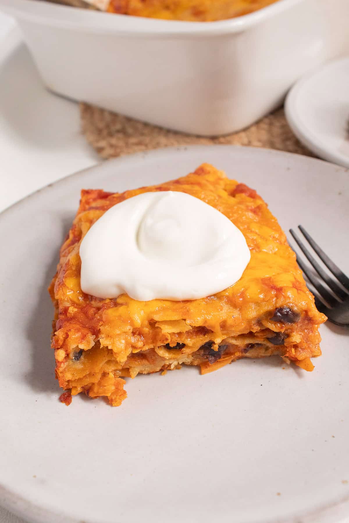 A serving of stacked enchiladas is topped with a dollop of sour cream.