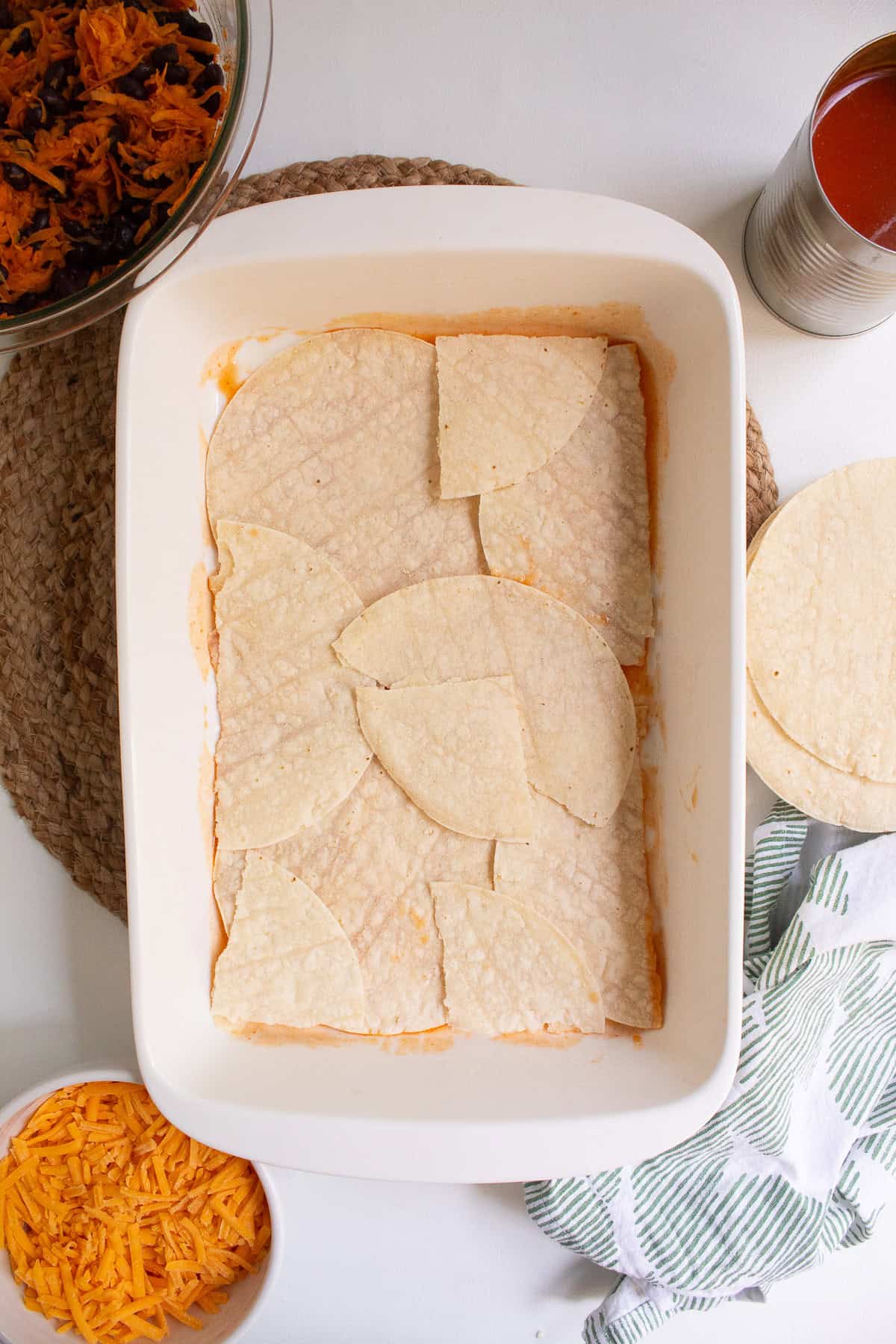 Torn tortillas form an even layer in the bottom of the casserole dish.