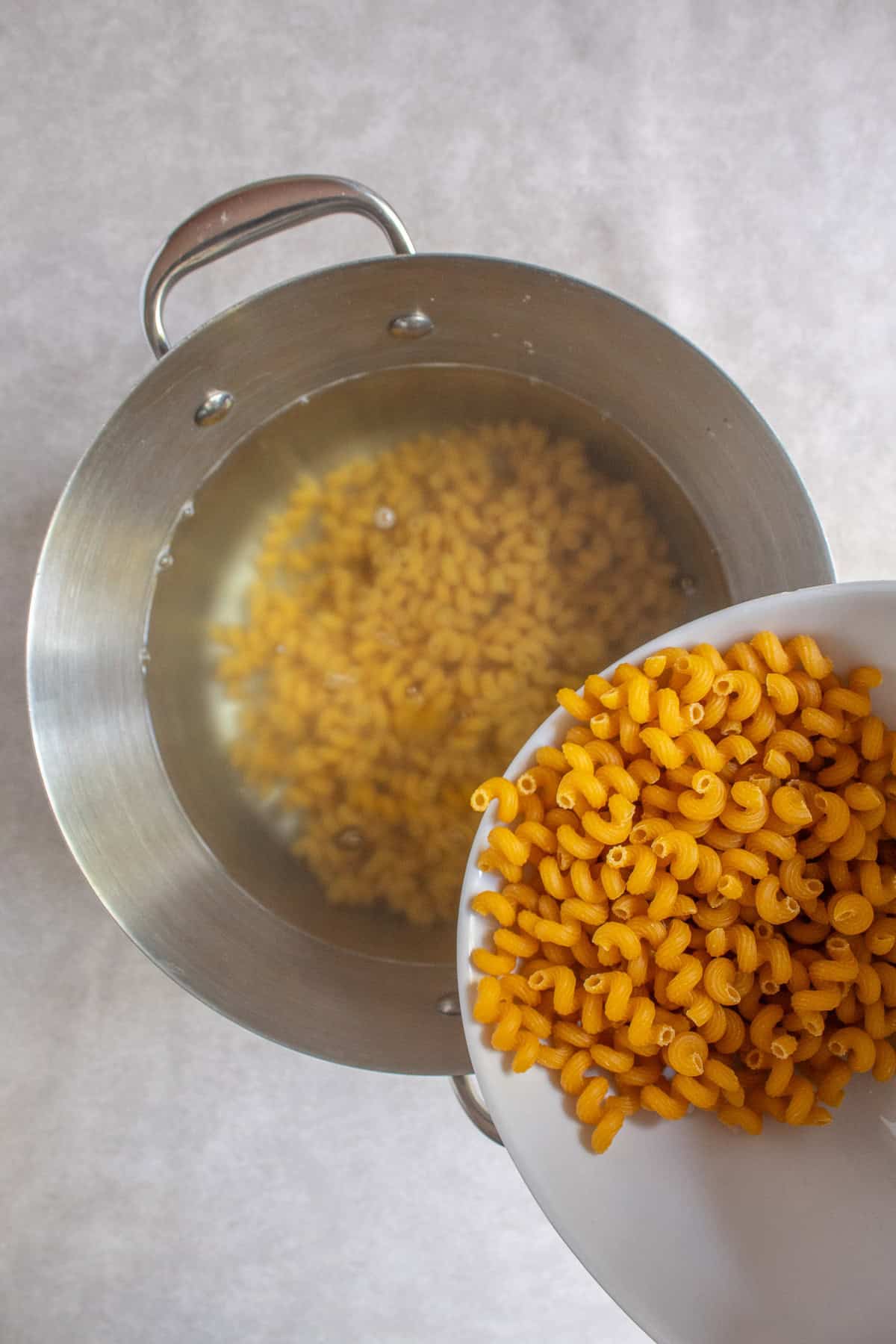 Curly macaroni pasta is added to boiling water in a large pot.
