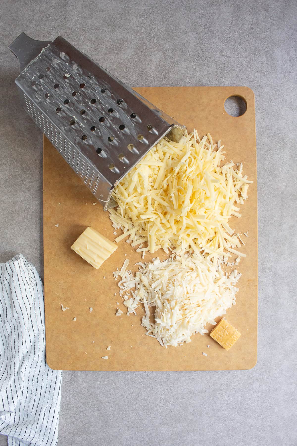 Gruyère and Parmesan cheeses are shredded on the large holes of a box grater.
