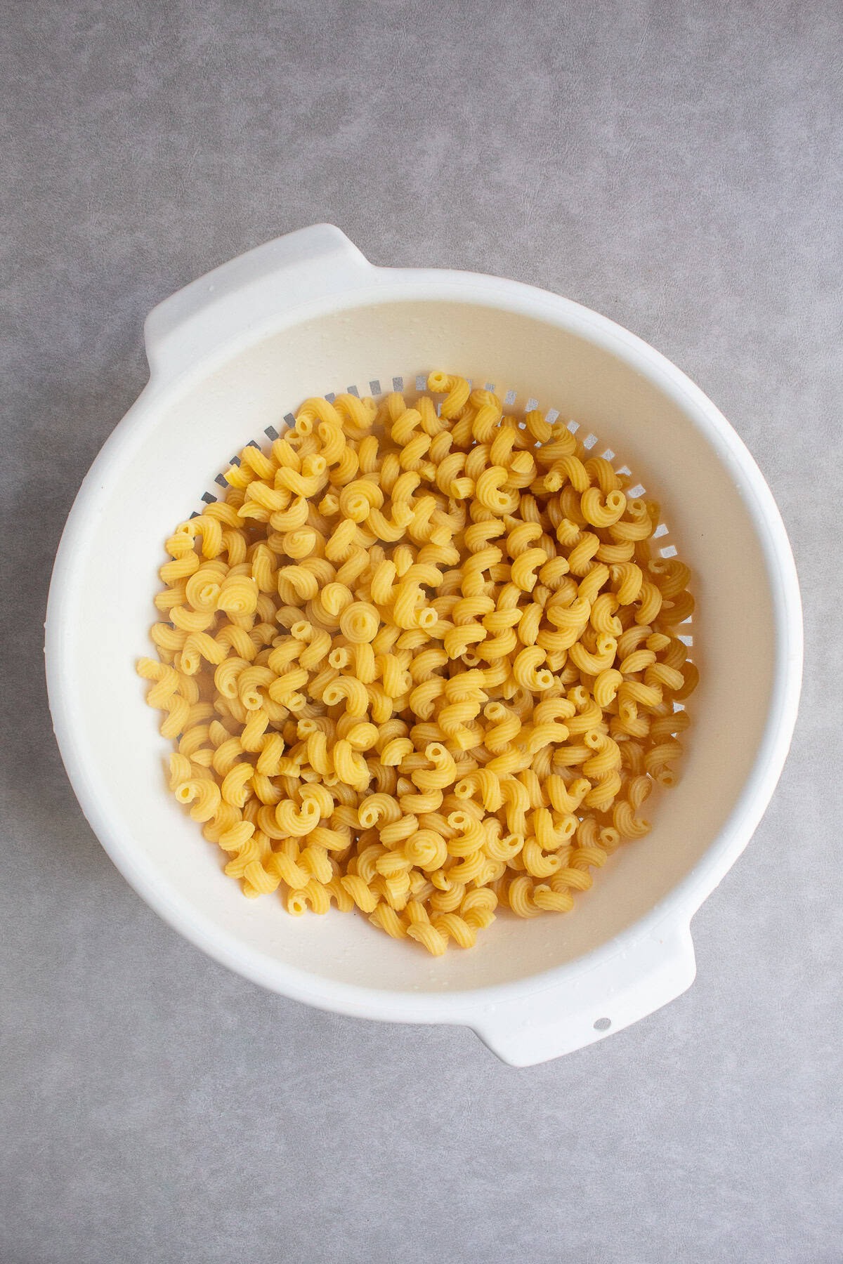 The cooked pasta is draining in a white colander.