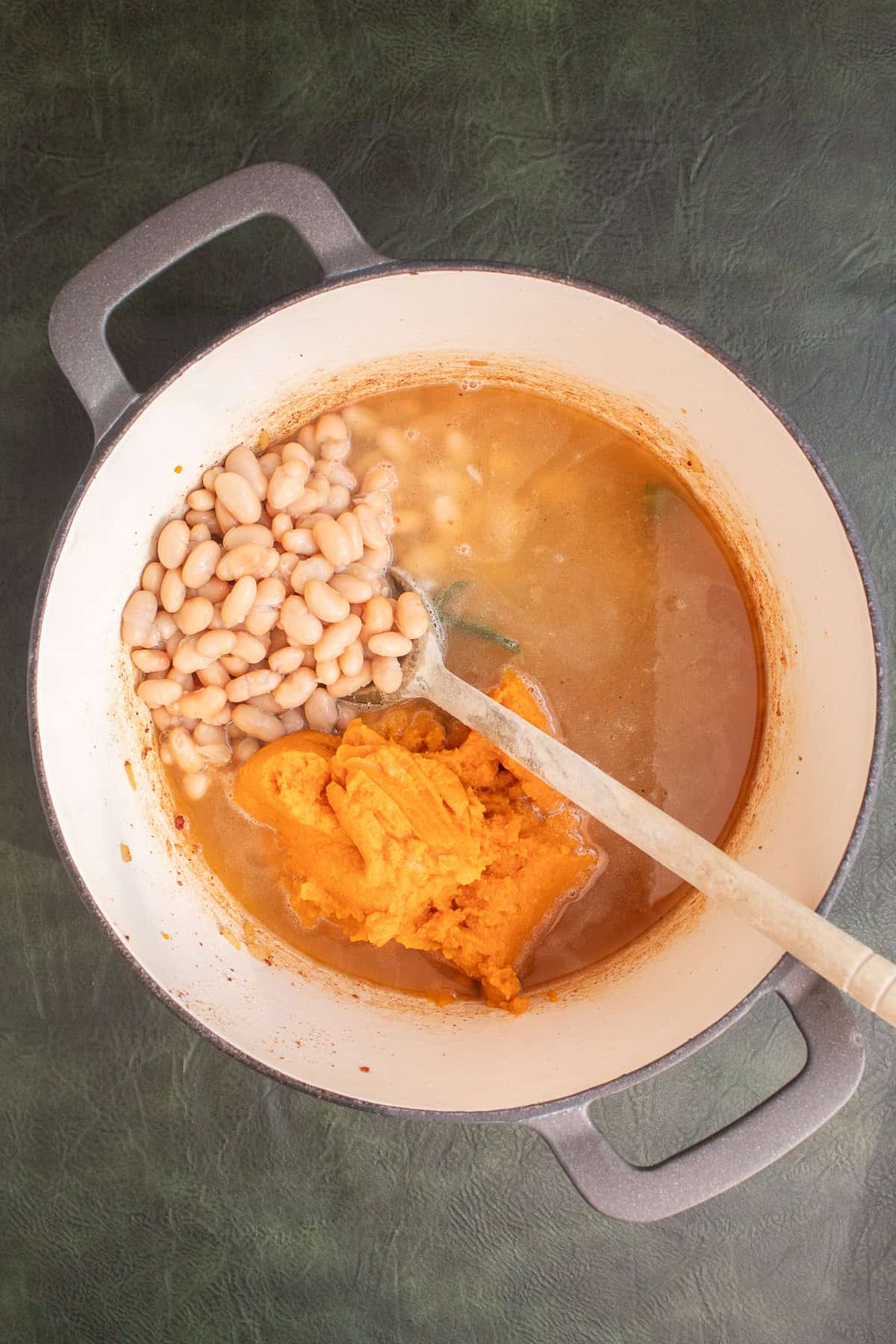 White beans and canned pumpkin are added to a soup pot along with chicken broth.