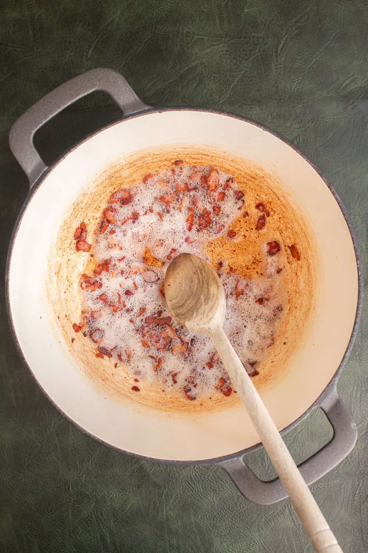 Chopped bacon is browning at the bottom of a large pot.