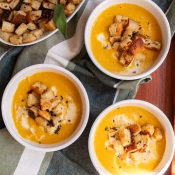 Three bowls of pumpkin soup are topped with sage and croutons.