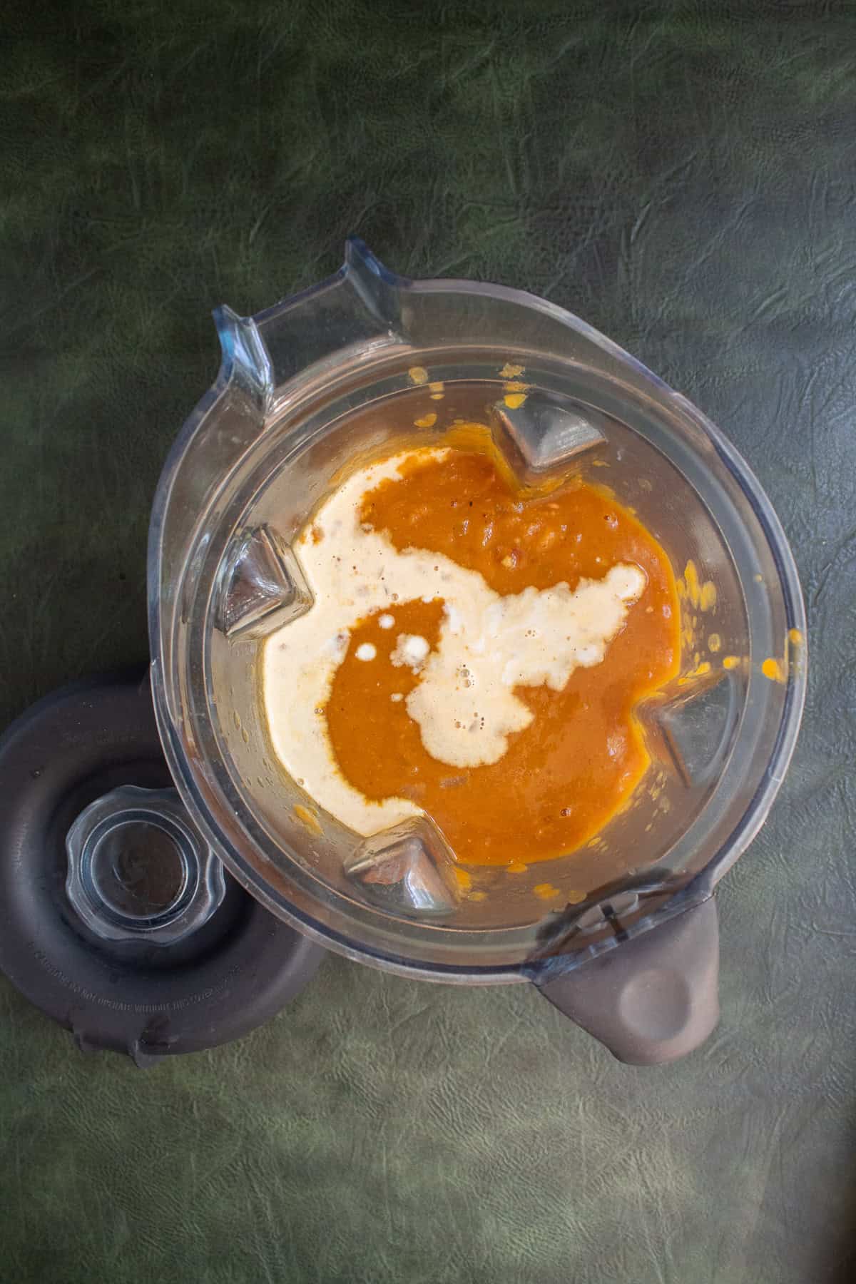 A blender pitcher is filled with a dark orange mixture and cream.