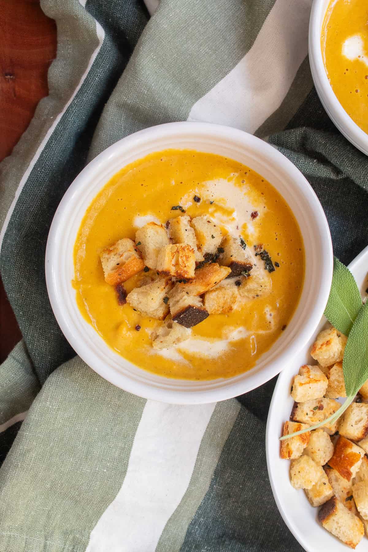 A white bowl of pumpkin soup is topped with golden croutons.