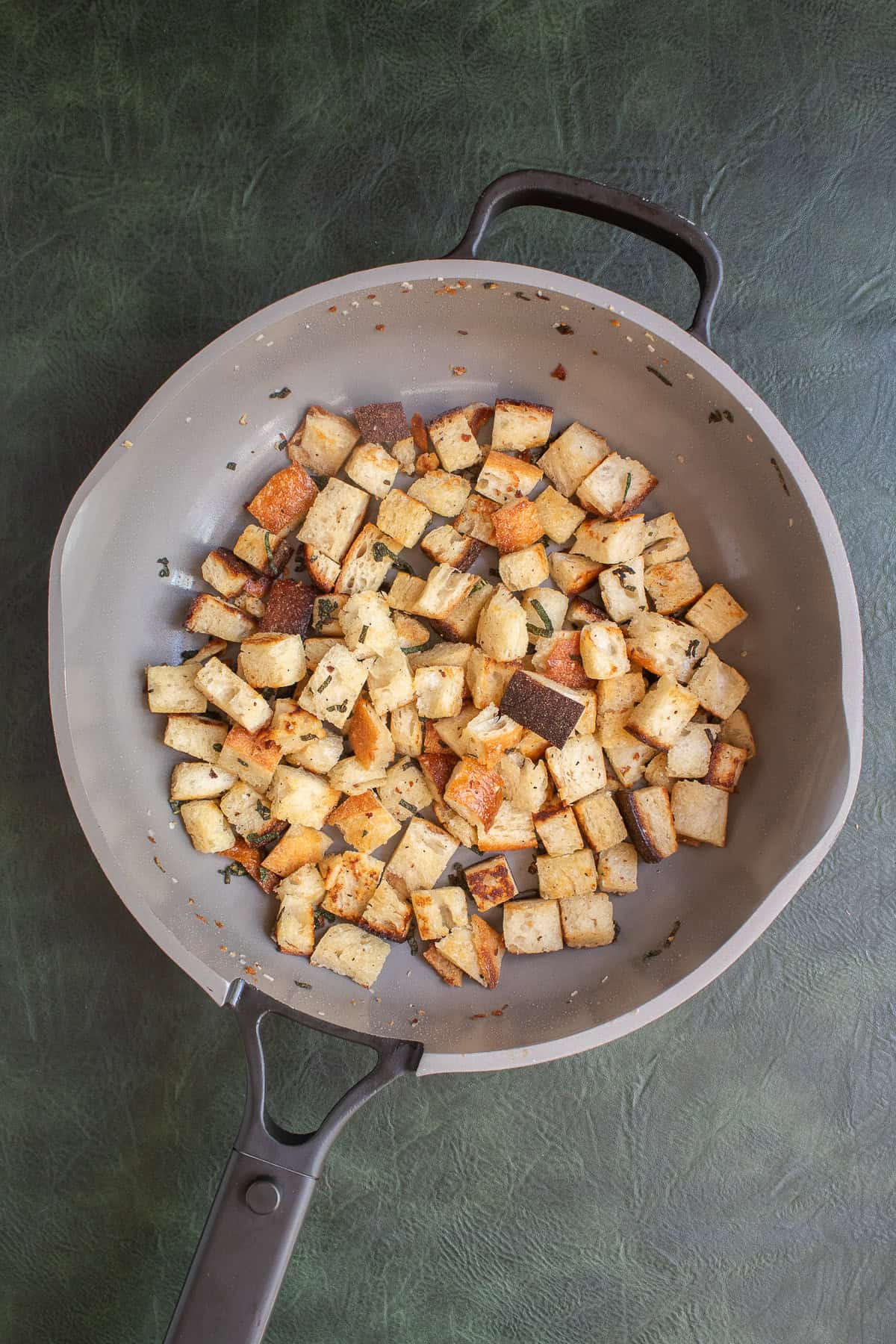 A gray skillet contains cubed bread and sage leaves that have been fried to a golden color.